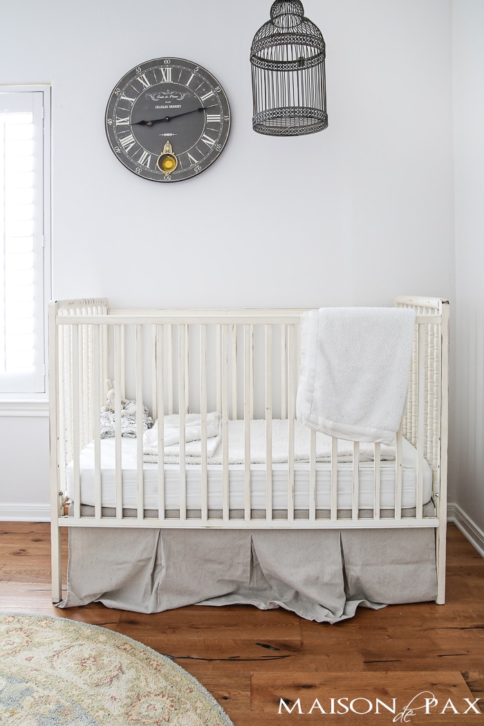 antique white spindle crib with large gray clock and birdcage hanging above - neutral, romantic, and lovely!
