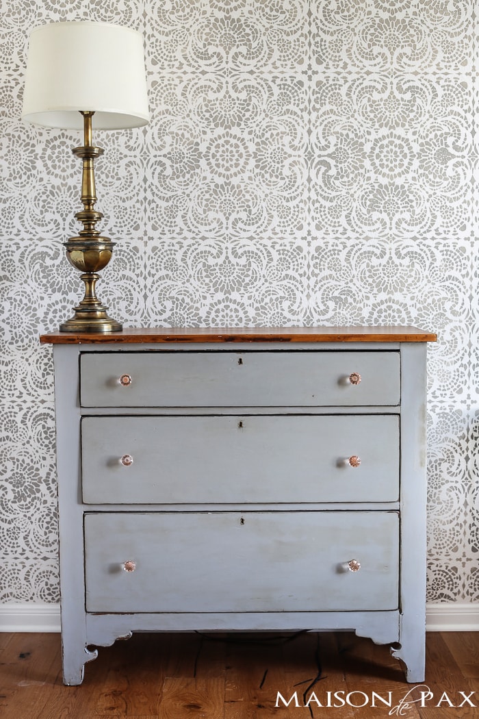 gray painted dresser with pink glass knobs and large, vintage brass lamp are perfect in front of this gray and white accent wall
