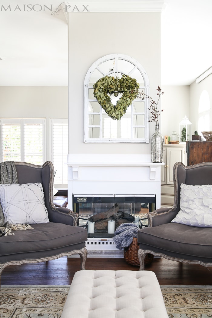 beautiful, neutral living room with gray wingback chairs, natural textures, white fireplace, and a gorgeous wreath 