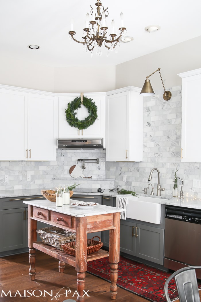 Gorgeous two-tone kitchen design with white upper cabinets, gray lower cabinets, carrara marble counters and marble subway tile backsplash, a farm sink, and a beautiful wood island and brass hardware...