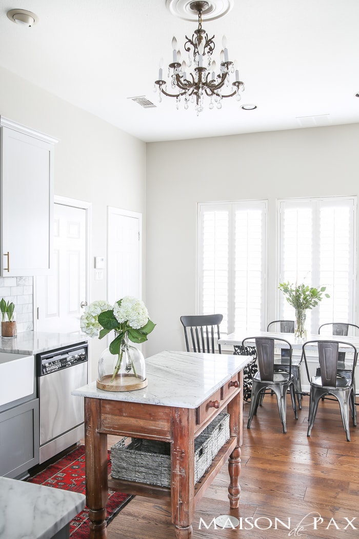 Two-toned gray and white cabinets, marble subway tile, Carrara countertops, a big farmhouse sink, and brass hardware give this kitchen a classic yet modern look.