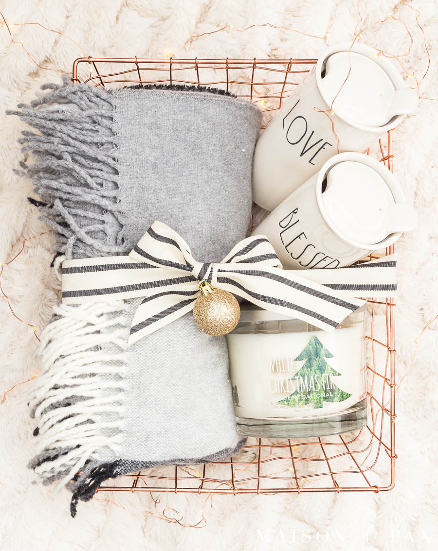fringed wood throw blanket, travel mugs, and holiday candle in a copper wire gift basket tied with a bow