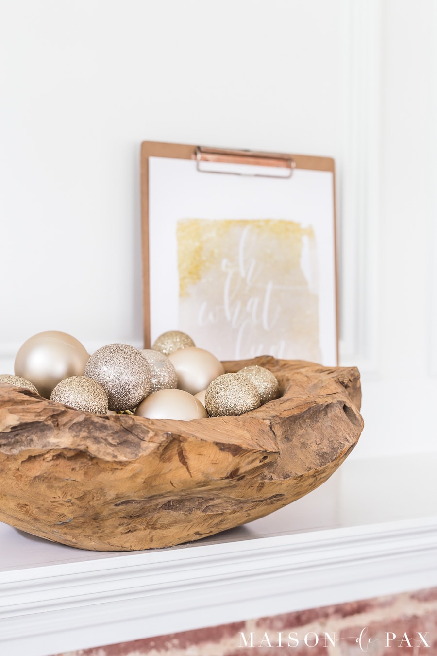 raw wood bowl of sparkly blush and gold ornaments on a white mantel
