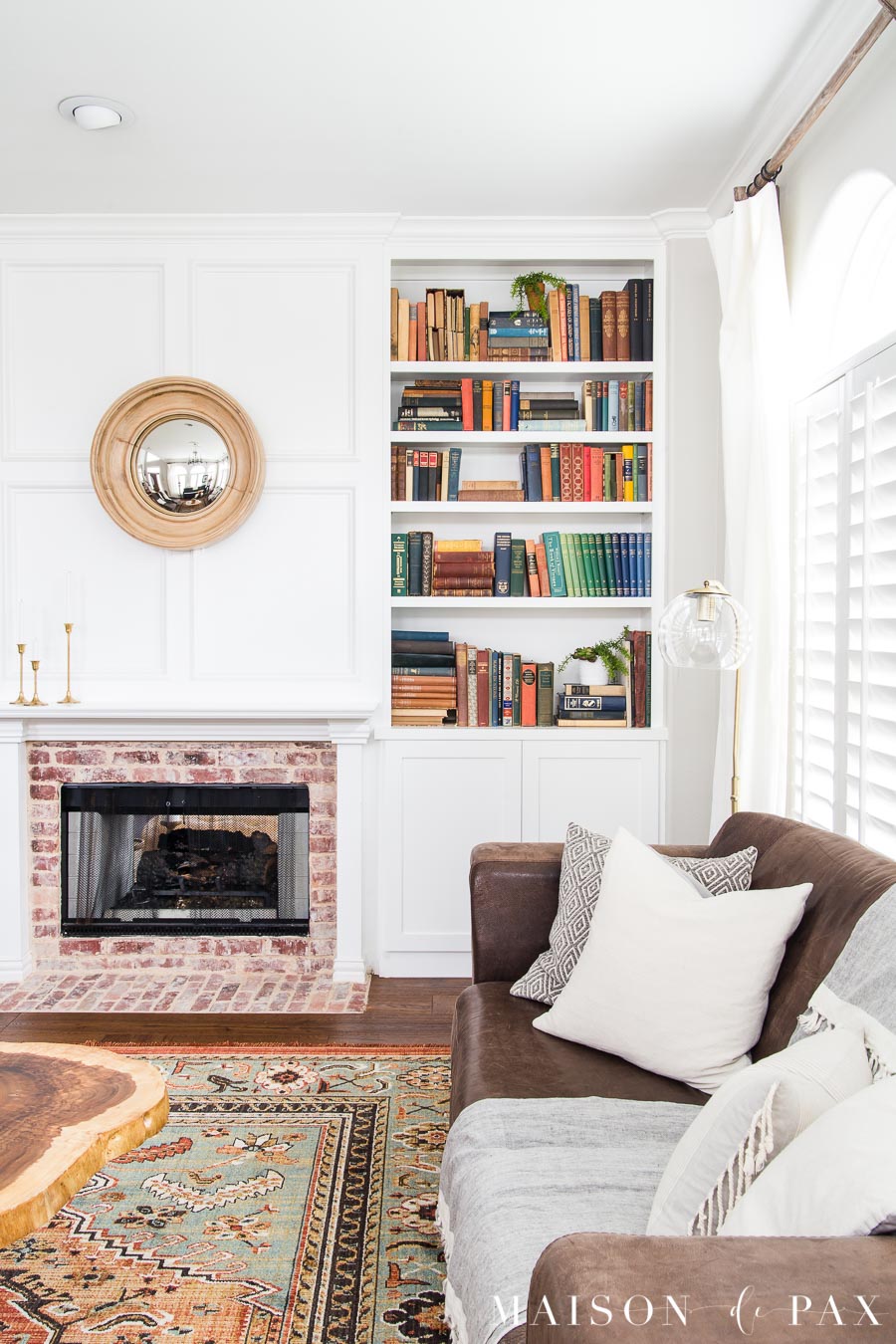 brown leather couch with white fireplace and colorful bookcase | Maison de Pax