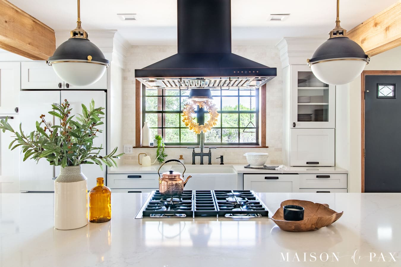 white kitchen island with stove top and large pendant lights | Maison de Pax