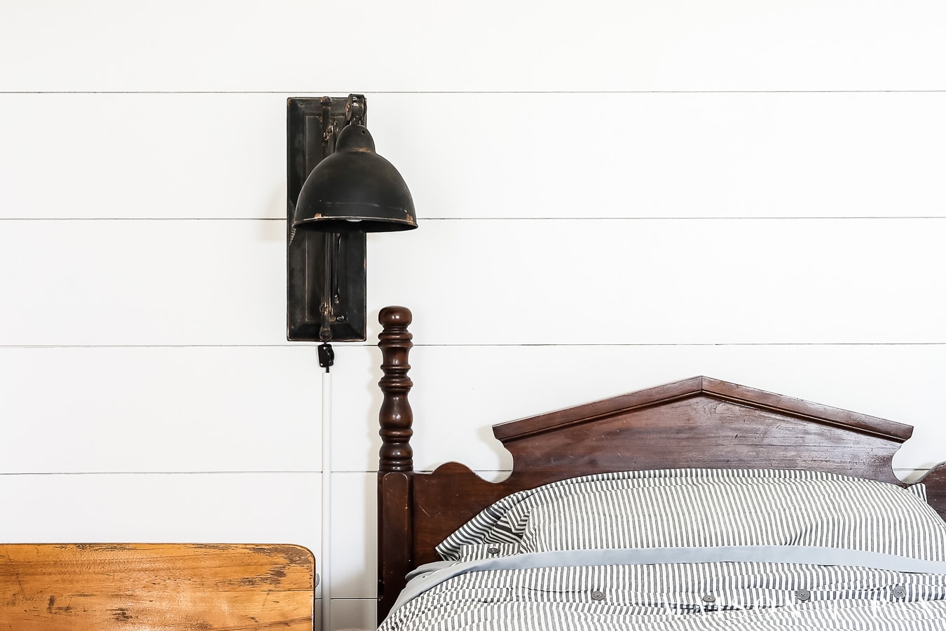 black modern farmhouse sconce beside vintage bed on planked wall