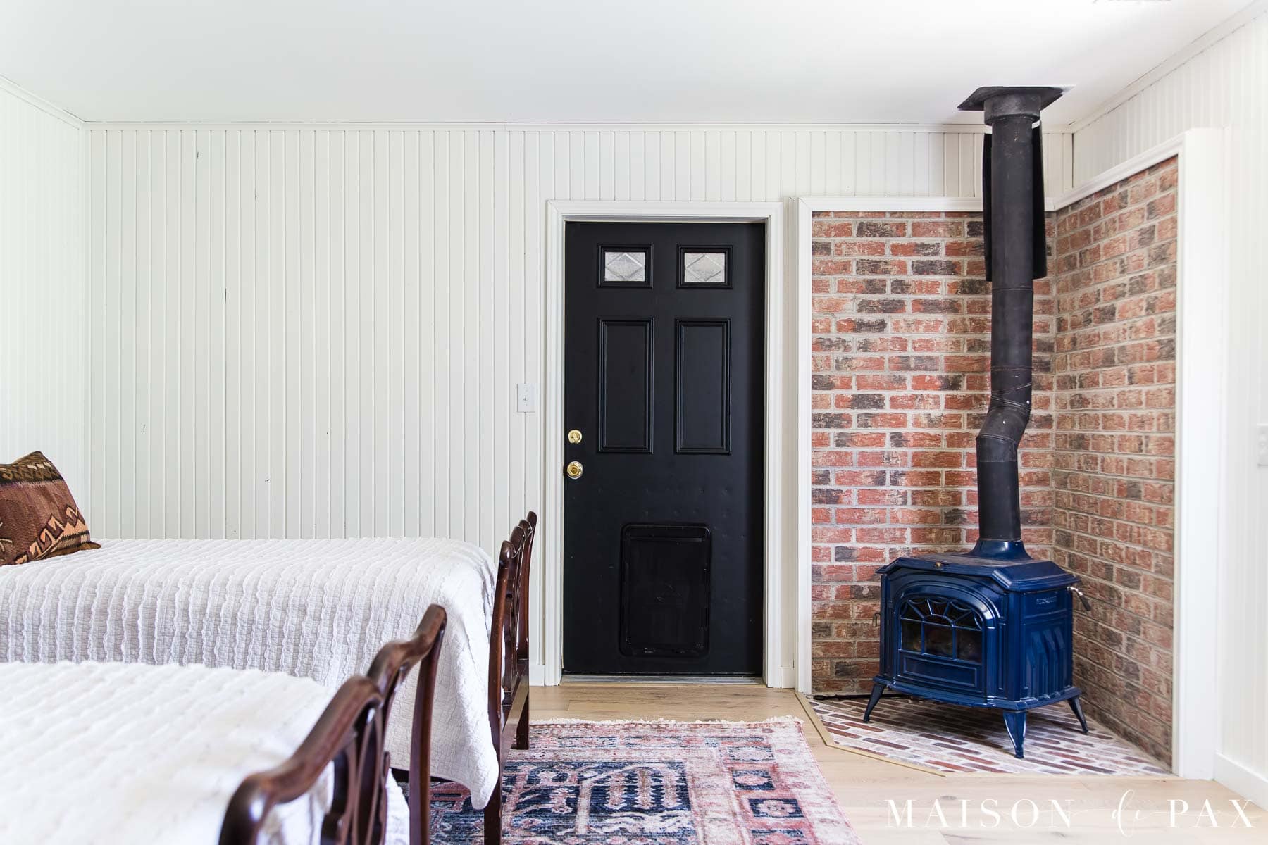 wood paneling painted white with black door and pot belly stove | Maison de Pax