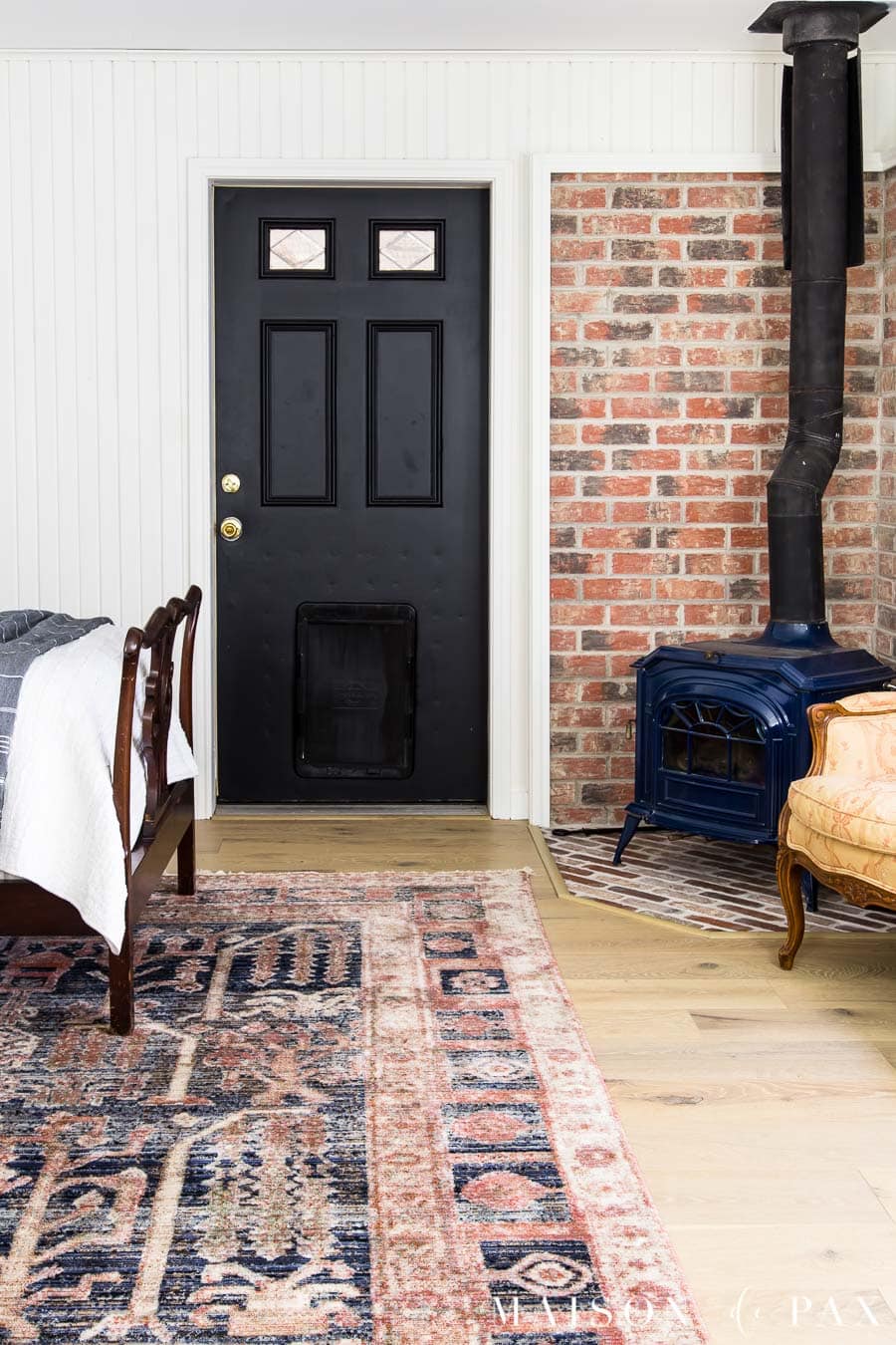 bedroom with black door, white planked walls, brick accent, pot belly stove | Maison de Pax