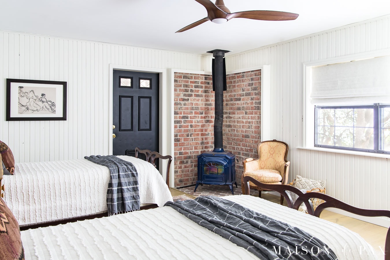 white farmhouse bedroom with planked walls, twin beds, black door, and pot belly stove | Maison de Pax