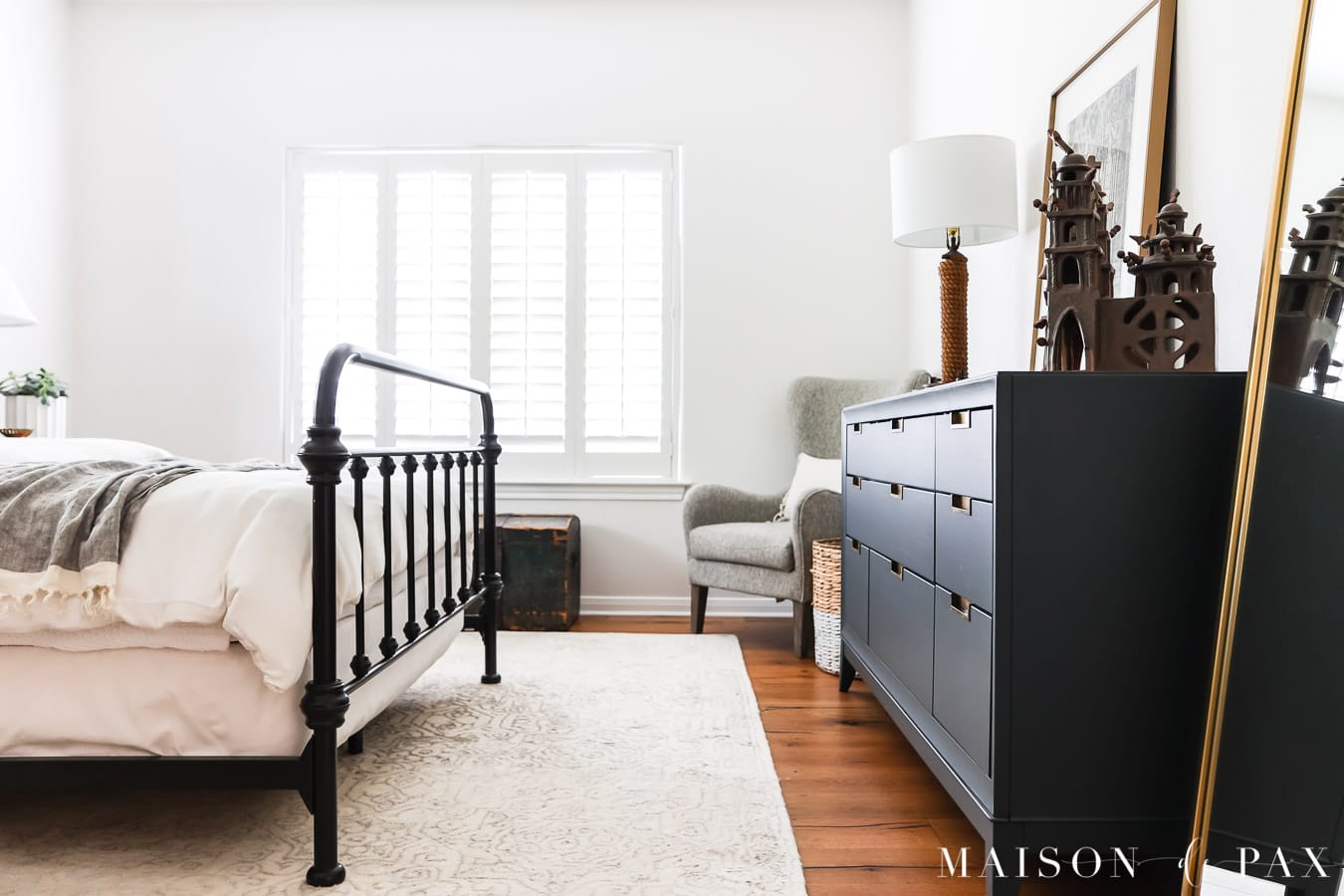 white bedroom with dark blue dresser and iron bed