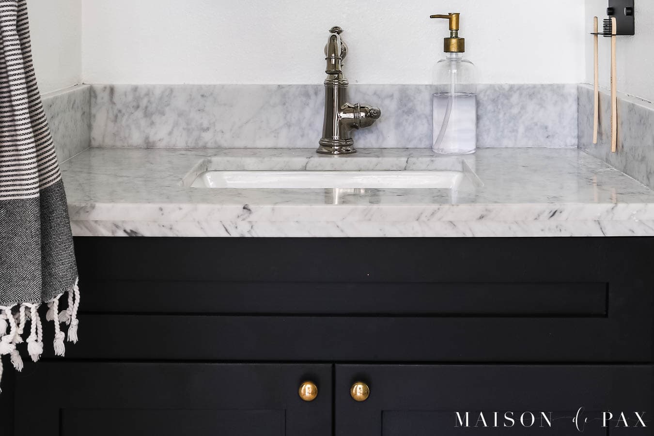 unlacquered brass knobs on black bathroom vanity with marble counter and polished nickel faucet