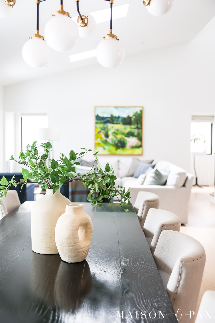 Open concept dining and living room with Sherwin Williams Pure White walls, black dining table, brass chandelier, and soft neutral furnishings