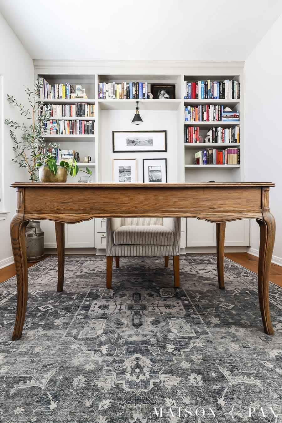 antique oak desk floating in home office in front of painted bookcases