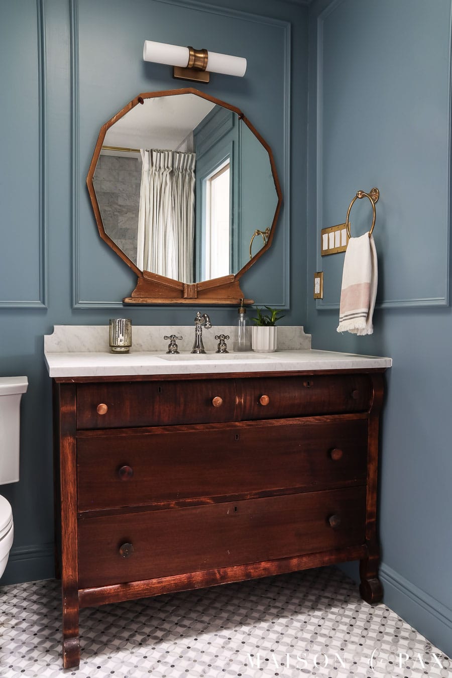 Blue bathroom with box trim on walls, wood vanity, and gold accents