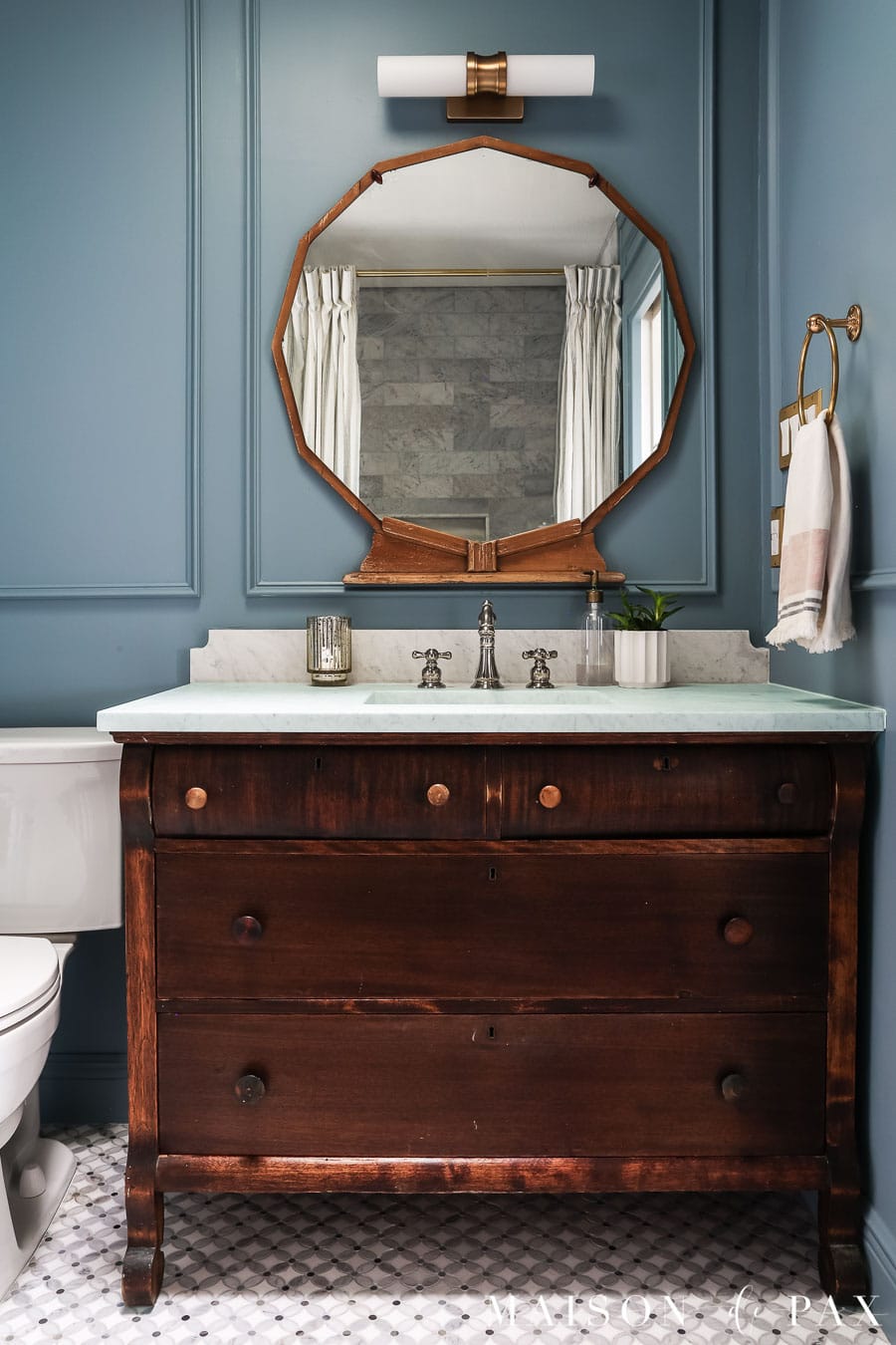 elegant small bathroom with wood vanity, marble top, blue walls, and vintage mirror