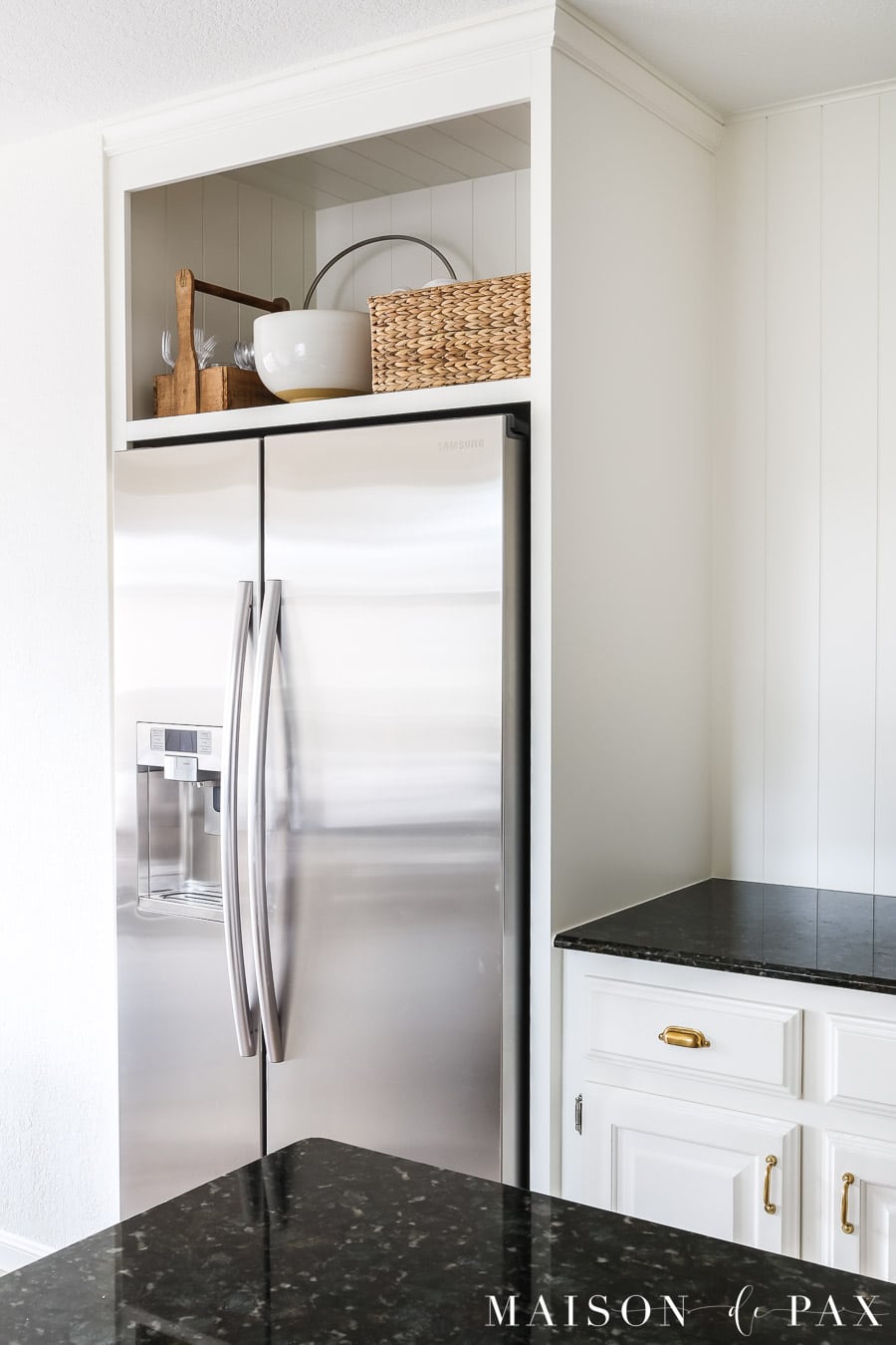 Kitchen corner with Sherwin Williams Alabaster walls, black countertops, white cabinetry, and stainless steel refrigerator