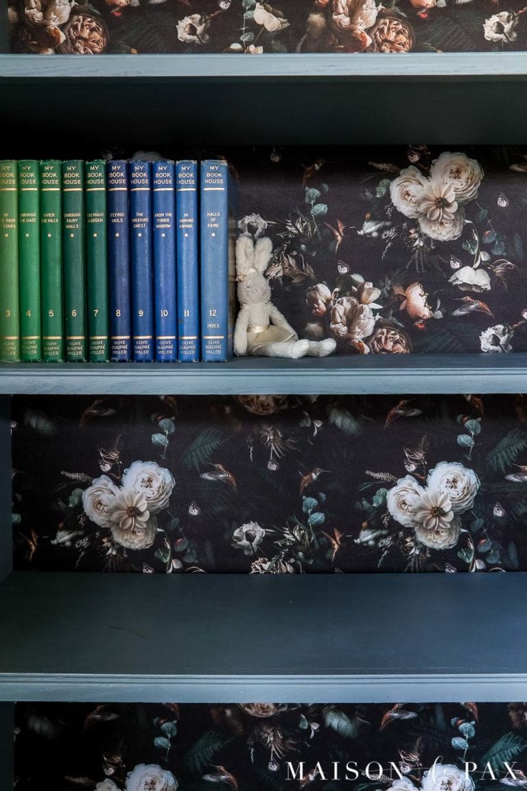 painted blue bookcase with black and floral wallpaper on back of shelves