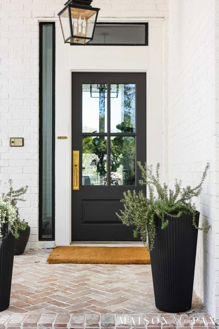 Sherwin Williams Iron Ore front door on white painted brick exterior with black planters and brass hardware