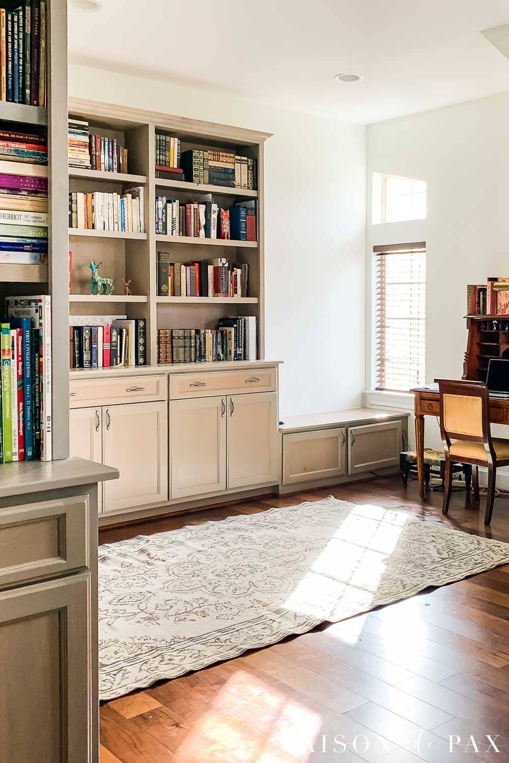 South-facing room with Sherwin Williams Alabaster walls, taupe built-in bookshelves, and warm wood floors in natural sunlight