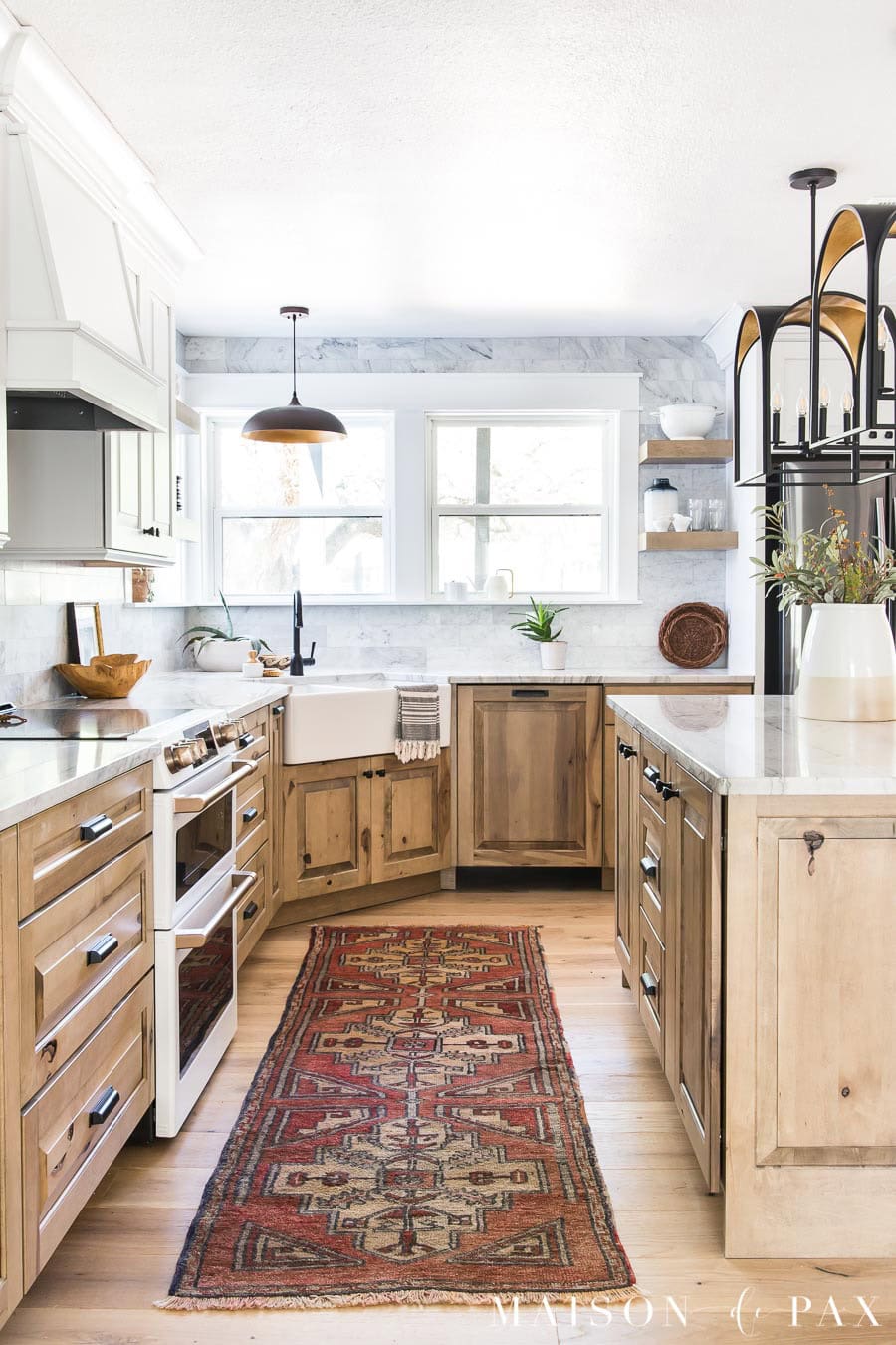 Updated 1980s kitchen with warm wood cabinets, white marble countertops, farmhouse sink, black lighting, and timeless finishes.