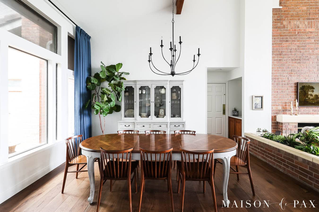 Updated 1980s dining room with vaulted ceiling, exposed wood beam, large windows, dark wood flooring, and collected furniture.
