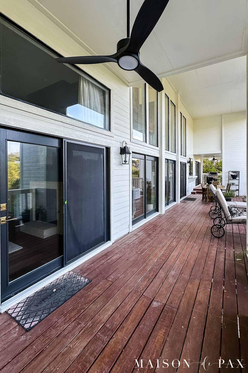 Long covered porch with freshly painted white exterior walls and an older faded reddish-brown stained wood deck before refinishing.