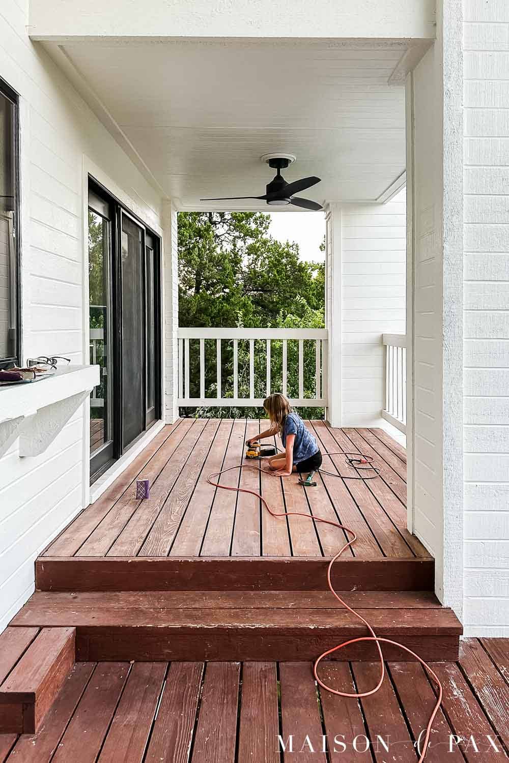 Previously stained wood porch being lightly sanded to prepare the faded reddish-brown finish for solid stain.