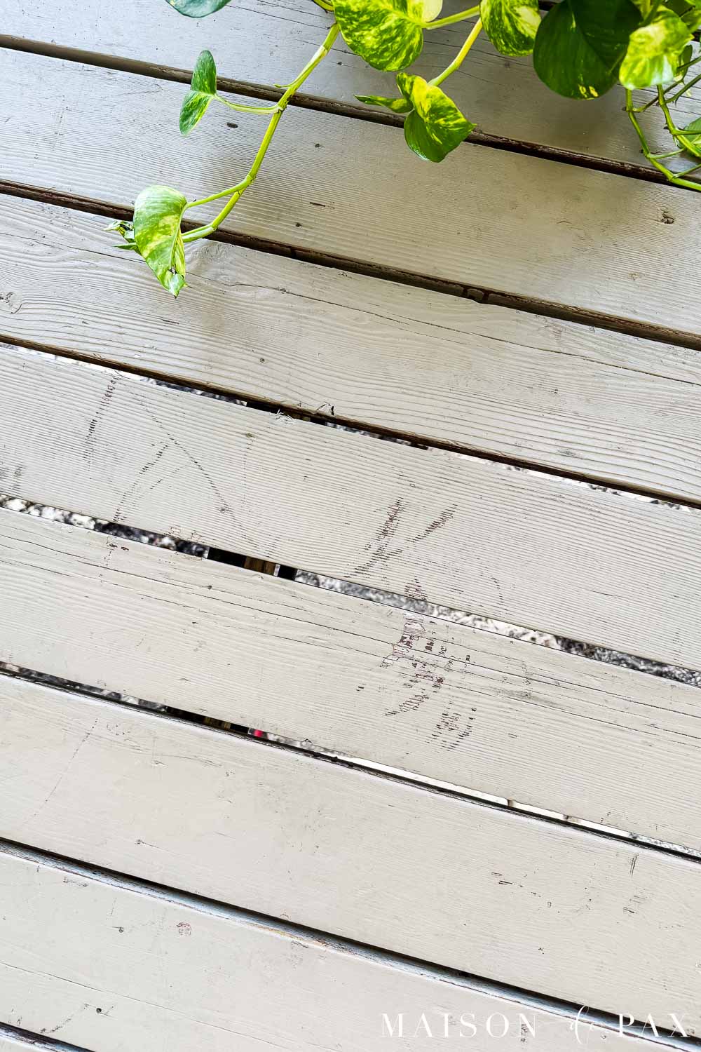 Close-up of warm beige solid-stained deck boards after 14 months showing scratches and scuffs that reveal some of the darker reddish stain underneath.